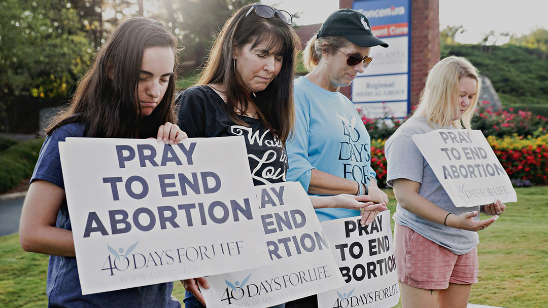 40Days-for-Life-4-People-Praying-on-Grass-with-Signs-1080x608 - Pikes Peak Citizens for Life